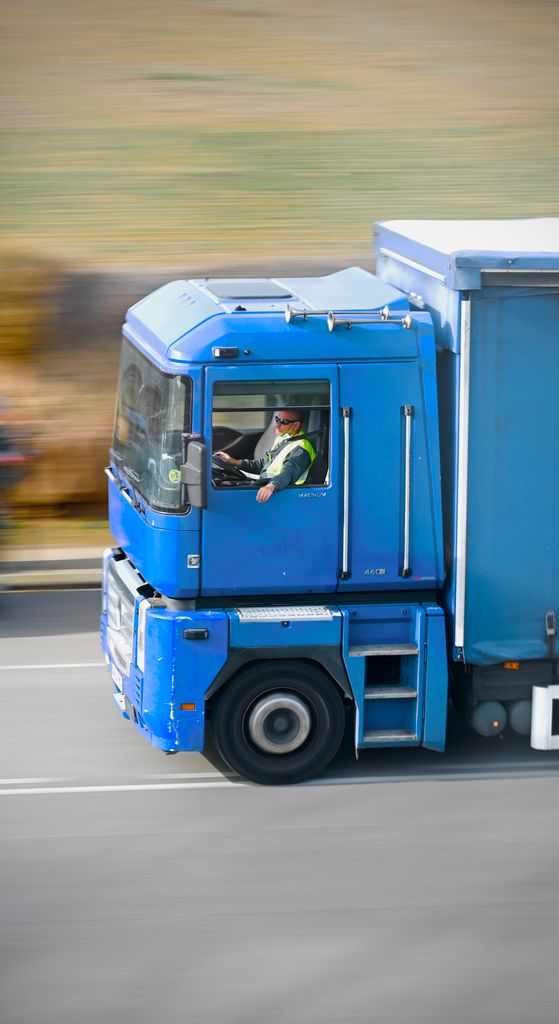 Dynamic panning shot capturing a blue truck in motion on a highway in daylight.